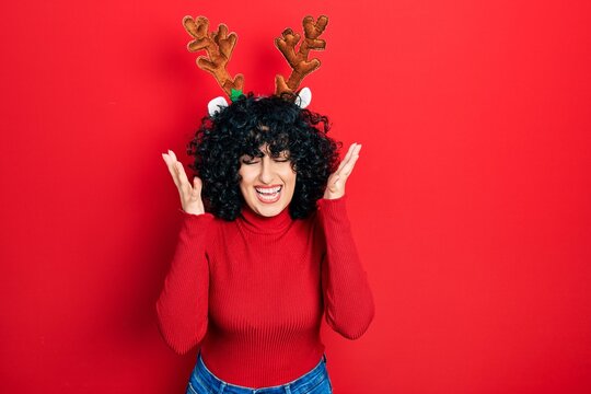 Young middle east woman wearing cute christmas reindeer horns celebrating mad and crazy for success with arms raised and closed eyes screaming excited. winner concept