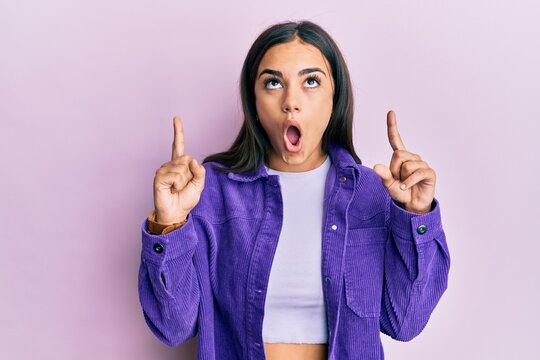 Young brunette woman wearing casual clothes amazed and surprised looking up and pointing with fingers and raised arms.