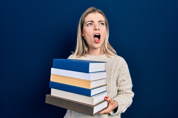 Beautiful caucasian woman holding a pile of books angry and mad screaming frustrated and furious, shouting with anger. rage and aggressive concept.