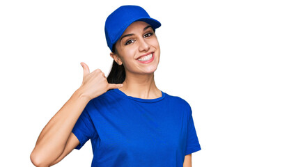Young hispanic girl wearing delivery courier uniform smiling doing phone gesture with hand and...