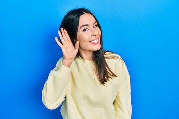 Fototapeta premium Young brunette woman wearing casual sweatshirt smiling with hand over ear listening an hearing to rumor or gossip. deafness concept.