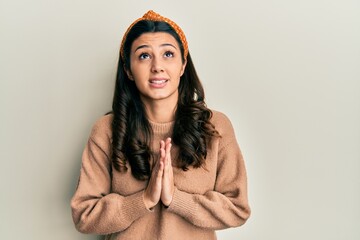 Young hispanic woman wearing casual clothes begging and praying with hands together with hope...