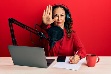 Beautiful middle age woman working at radio studio with open hand doing stop sign with serious and confident expression, defense gesture