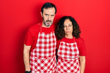 Middle age couple of hispanic woman and man wearing cook apron skeptic and nervous, frowning upset because of problem. negative person.