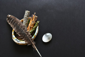 A top view image of healing smudge sticks and sacred feather on a black background. 