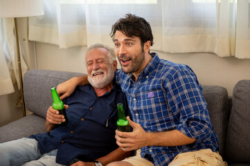 Happy Caucasian family senior father and adult son watching sport game on TV with drinking beer...