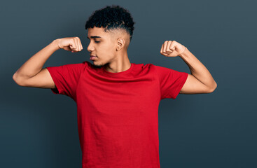 Young african american man wearing casual red t shirt showing arms muscles smiling proud. fitness concept.