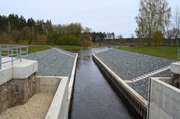 View of the source of the canal lock in the river, which is surrounded on both sides by a shore covered with white stones.