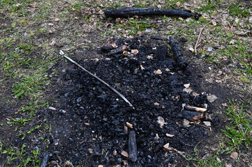 A fireplace in nature with burnt coals from logs and a metal skewer thrown into it.