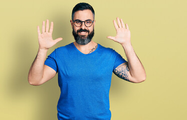 Hispanic man with beard wearing casual t shirt and glasses showing and pointing up with fingers number ten while smiling confident and happy.