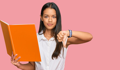 Beautiful hispanic woman reading book with angry face, negative sign showing dislike with thumbs down, rejection concept