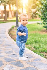 Fototapeta premium Cute and happy little boy having fun at the park on a sunny day. Beautiful blonde hair male toddler playing outdoors