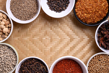 Various dry spices and herbs in a bowl on woven bamboo background. Asian food ingredients (chili, clove, caraway, coriander seed, star anise, cardamom and pepper)