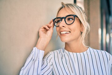 Young blonde businesswoman smiling happy leaning on the wall at the city.