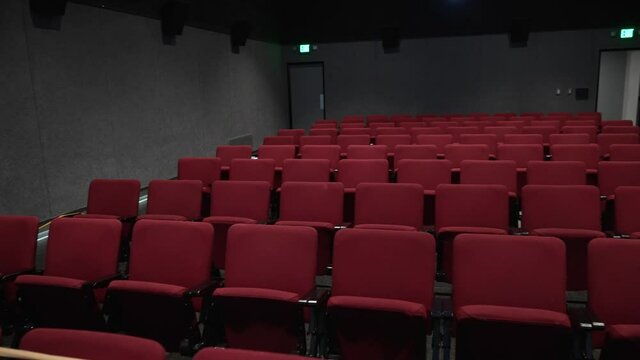 This panning video shows the front view of an empty movie theater with rows of unused red cinema seats.