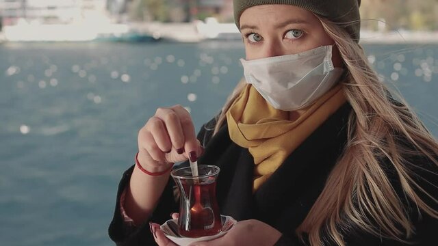 A woman's hand is holding a white cup of hot milky beverage with cinnamon called Turkish salep sahlep on the background of rippling water and misty Maiden s Tower in the distance, Istanbul.