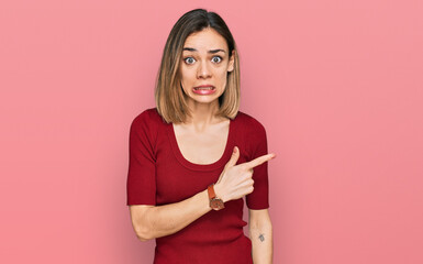 Young blonde girl wearing casual clothes pointing aside worried and nervous with forefinger,...