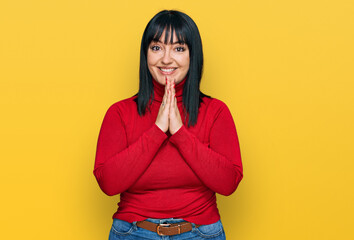 Young hispanic woman wearing casual clothes praying with hands together asking for forgiveness smiling confident.