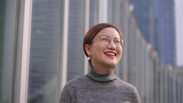 4k slow motion Confident young beautiful asian businesswoman walking in front of office building wearing glasses in sunny weather