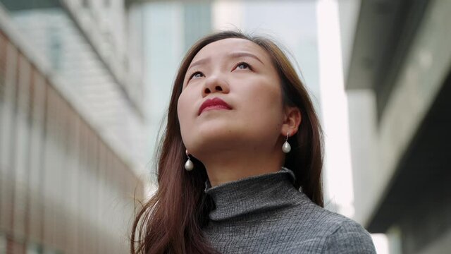 4k slow motion Low angle shot of confident serious Asian businesswoman looking around in front of urban office building