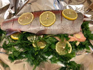 Raw red fish with lemons and herbs on foil.