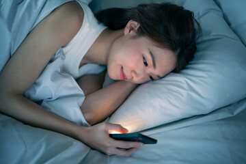 ベッドで寝ながらスマートフォンを見る女性