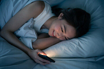 ベッドで寝ながらスマートフォンを見る女性 - obrazy, fototapety, plakaty