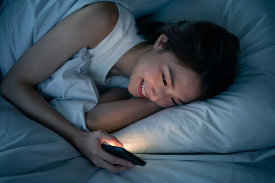 ベッドで寝ながらスマートフォンを見る女性