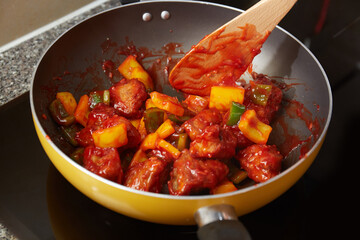 A closeup shot of a meal being cooked in a frying pan. Sweet and sour pork fried with vegetables