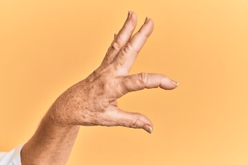 Senior caucasian hand over yellow isolated background picking and taking invisible thing, holding object with fingers showing space