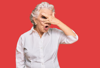 Senior grey-haired woman wearing casual clothes peeking in shock covering face and eyes with hand, looking through fingers with embarrassed expression.