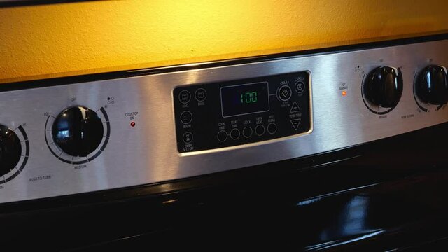 Womans hand regulating cooking on oven panel in kitchen. Woman setting temperature on control panel on modern electric oven appliance.