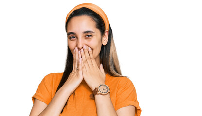 Young hispanic woman wearing casual clothes laughing and embarrassed giggle covering mouth with...