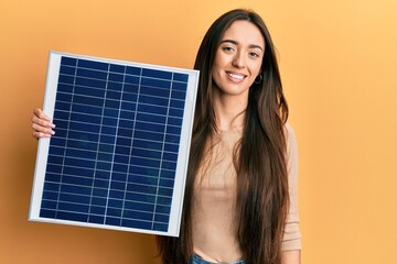 Young hispanic girl holding photovoltaic solar panel looking positive and happy standing and smiling with a confident smile showing teeth