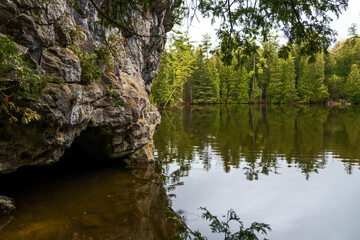 A small cave at the side of a lake in Rockwood Conservation Area near Guelph, Ontario, with a forest in the background.