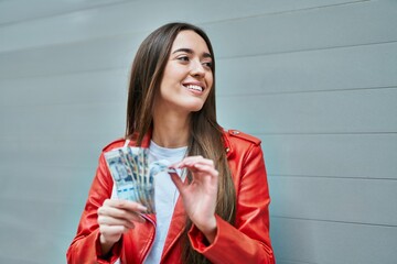 Young hispanic woman smiling happy counting peruvian sol banknotes at the city.