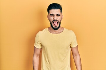 Handsome man with beard wearing casual yellow t shirt sticking tongue out happy with funny expression. emotion concept.