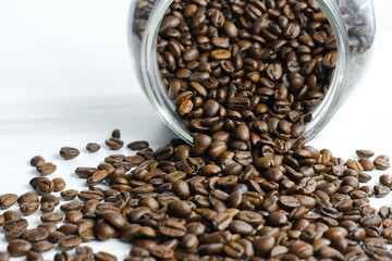 Spilled roasted coffee beans from glass jar on white table.  Coffee beans in a coffee shop for tasting.