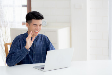 Fototapeta premium Young asian business man using laptop computer for video call online hello and communicate work from home, male conference with notebook and say hi, social distancing, communication concept.