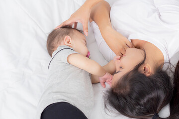 Fototapeta na wymiar Young asian mother touch head of little baby girl with tender on bed in the bedroom, mom love newborn and care, woman with expression with child together, parent and daughter, family concept.