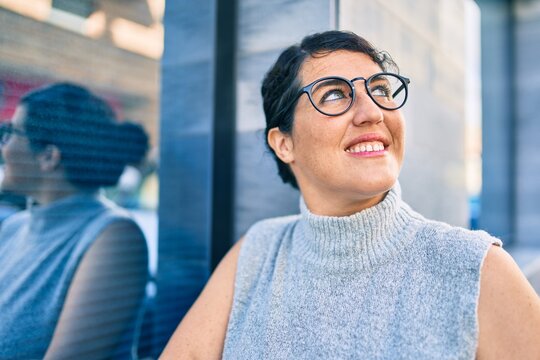 Young plus size woman smiling happy leaning on the wall at the city.