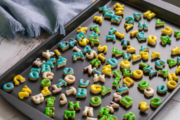plaque de cuisson avec quantité de biscuits en forme de lettres et crémage de couleur avec...