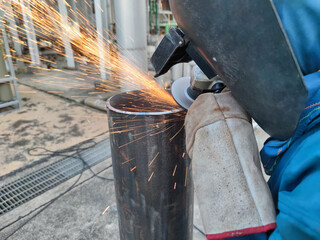 workers cutting metal sheets with electric grinder in the workshop. Welder is wear personal protective equipment(PPE) while working. Leather gloves and face shield.