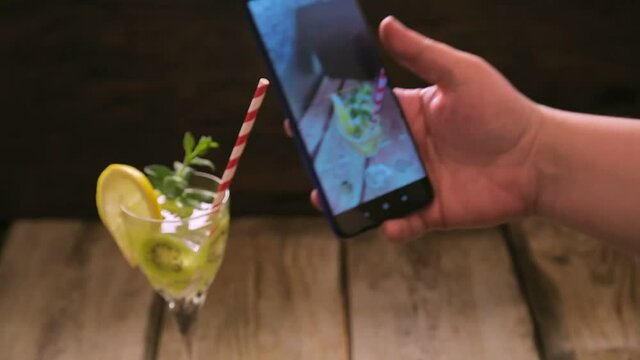 Cocktail with mint cucumber and lemon in a glass female hand takes a picture on a smartphone