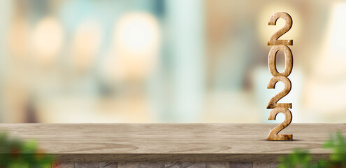 New year 2022 (3d rendering) on brown wood table at blur abstract bokeh light home background with blur leaf foreground,Mock up banner for display of product,holiday celebration greeting card
