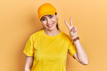 Young hispanic woman wearing delivery uniform and cap showing and pointing up with fingers number two while smiling confident and happy.