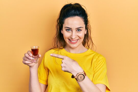 Young hispanic woman drinking whiskey shot smiling happy pointing with hand and finger