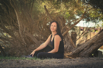 Brunette woman wearing black sitting on ground with Australian paperbark tree in background