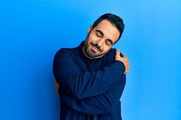 Young hispanic man wearing casual clothes hugging oneself happy and positive, smiling confident. self love and self care