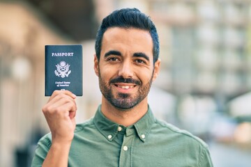 Young hispanic man smiling happy holding united states passport at the city.